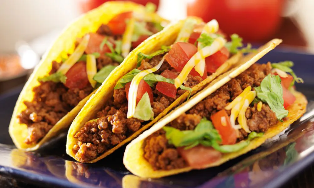 Three beef tacos with cheese, lettuce, and tomatoes on a blue plate at Acbento, a Fast Food Restaurant in Flushing
